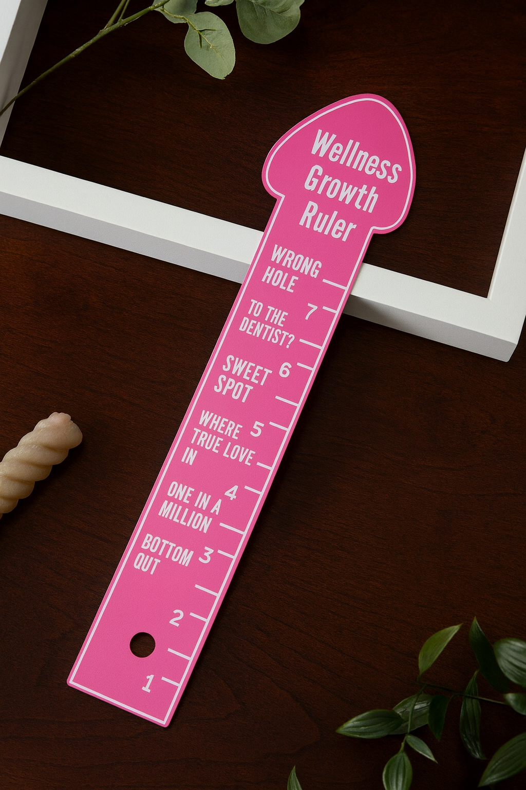 Pink eggplant ruler for couples measuring wellness growth with humorous markings on wooden surface
